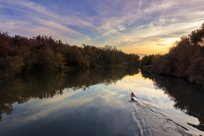 Rear view of person traveling in boat on river against sky during sunset