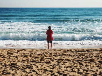 Rear view of boy on beach against sky