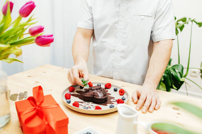 Close-up of a man's hands decorating a chocolate heart cake with a sprig of fresh mint 