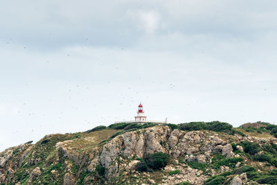 Lighthouse on rock by building against sky