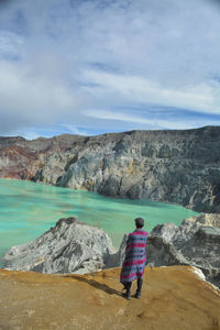 Rear view of woman on rock by mountains against sky