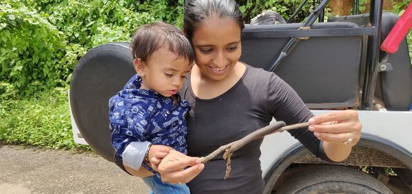 Mother and son looking at centipede on stick against vehicle