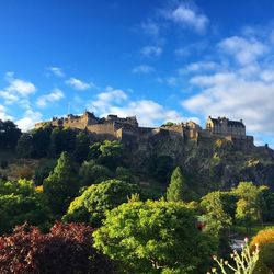 Low angle view of edinburgh castle and trees against cloudy blue sky