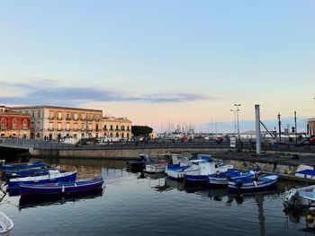 Boats moored in harbor at sunset