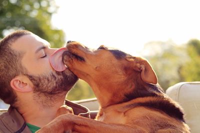 Dog licking owner against clear sky