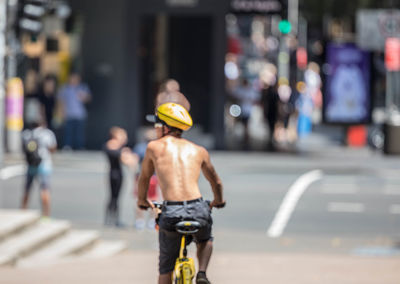 Rear view of shirtless man riding bicycle on road at city