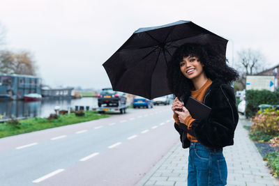 Portrait of young woman with umbrella standing against sky