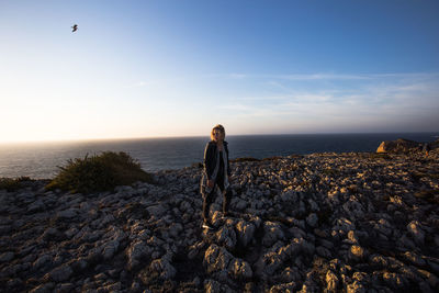 Man standing on rock by sea against sky