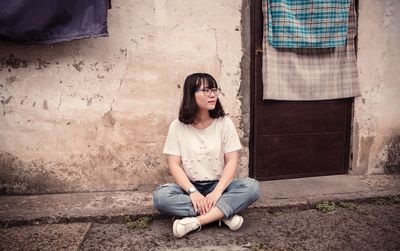Young woman sitting on floor against wall