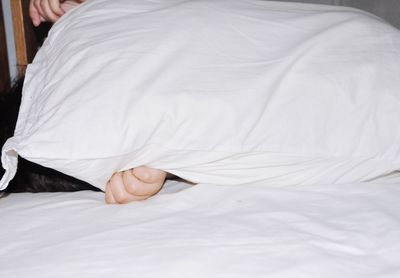 Close-up of woman covering with pillow on bed