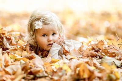 Portrait of cute girl lying on dry leaves during autumn