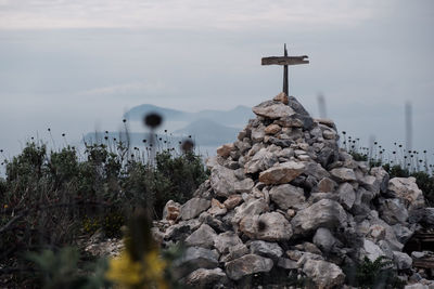 Cross on rock by building against sky