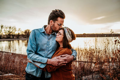 Hip husband kissing smiling wife near a lake in colorado