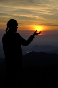 Silhouette man standing against orange sky during sunset