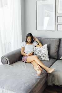 Girl reading book sitting on sofa at home