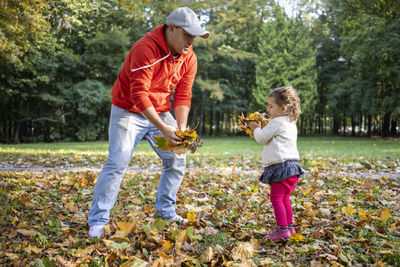 Little toddler girl plays with father outdoors in autumn park