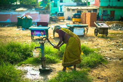 Full length of senior woman in sari using water pump