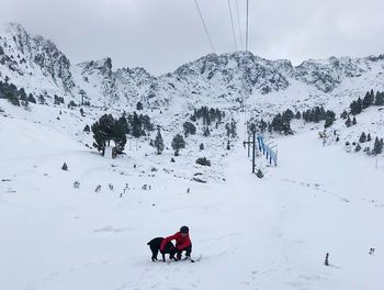 Woman with dog on snow covered field against sky