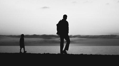 Silhouette men walking on beach against sky