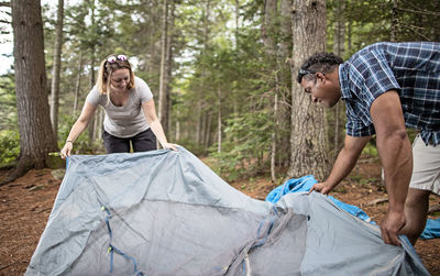 Multi racial couple set up tent in woods on appalachian trail, maine