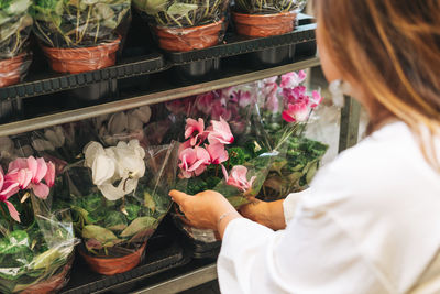 Brunette middle aged woman in white dress buys pink flower potted house plants at garden store
