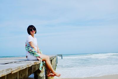 Woman in sunglasses sitting on pier over sea against sky