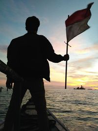 Silhouette man standing by sea against sky during sunset