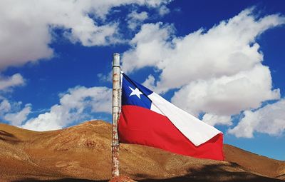 Low angle view of flag of chile on mountain against blue cloudy sky