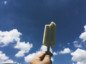 Cropped hand holding ice cream against sky