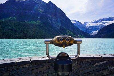 Close-up of coin-operated binoculars by lake against mountains