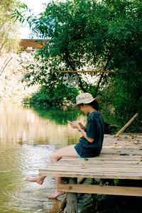 Side view of woman sitting on bench at lake