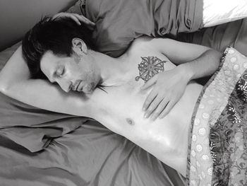 High angle view of tattooed man sleeping on bed at home