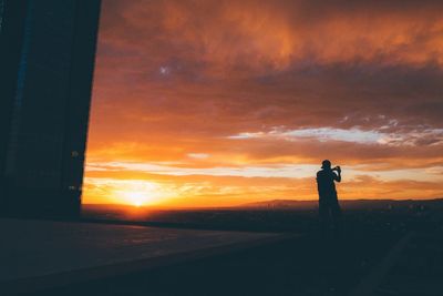 Silhouette of man photographing sunset sky over sea