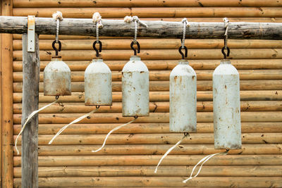 Many modern church bells hanging outside on the background of a wooden wall.