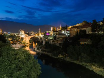 Illuminated buildings by river against sky at night