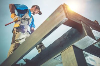 Low angle view of man working on railing against sky