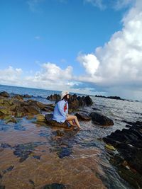 Man sitting on rock at beach against sky