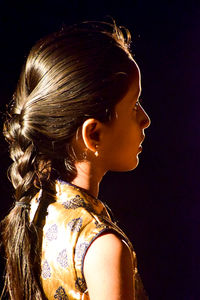 Side view portrait of a young woman against black background