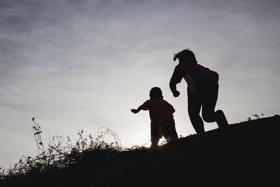 Silhouette friends standing on land against sky during sunset