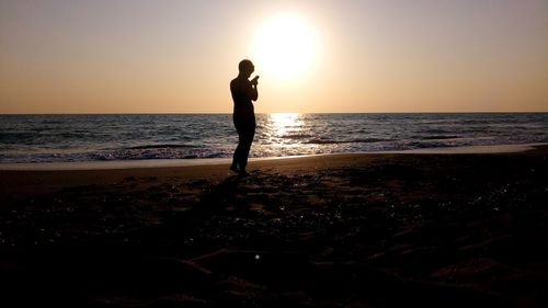 Silhouette woman standing at beach against sky during sunset