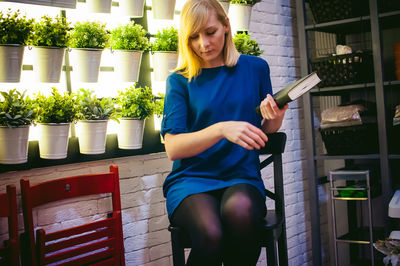 Young woman holding book against potted plants at greenhouse