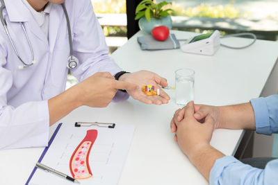 Midsection of doctor giving medicine to patient at clinic