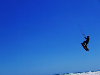 Low angle view of man paragliding against clear blue sky