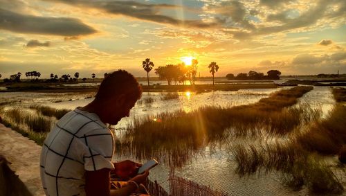 View of man at the pond edge under the sky during sunset