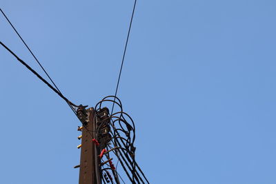 Low angle view of electricity pylon against clear blue sky