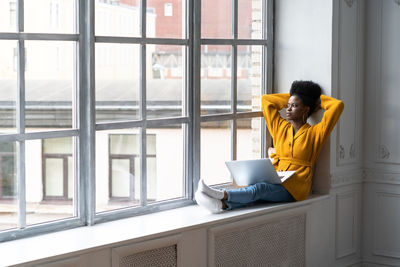 Young woman with laptop sitting by window at home