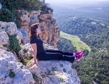 Full length of young woman resting on rocky cliff