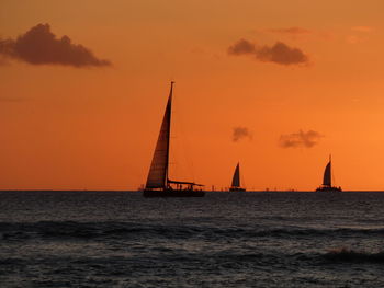 Silhouette sailboat sailing on sea against orange sky