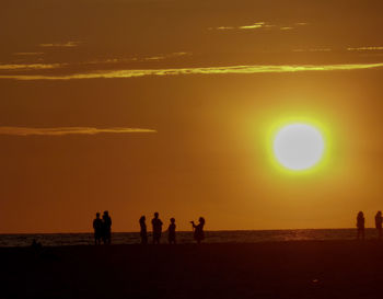 Silhouette people on beach against sky during sunset