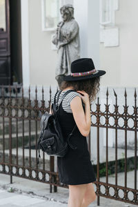 Rear view of woman wearing hat standing against railing